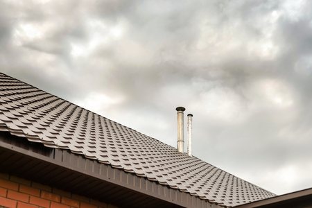 Two air vents on a home roof for purging gas and air from a house sit on a brown metal rooftopの写真素材