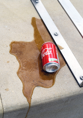 Spilt coke can on concrete with a brown liquid flow of cola on the surfaceの写真素材