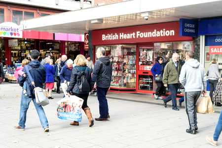 British shoppers in daytime walk past a British Heart Foundation charity shop in Chelmsford Essexのeditorial素材