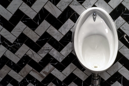 Single white male urinal in white porcelain with a tiled pattern in black and white in herringbone styleの写真素材