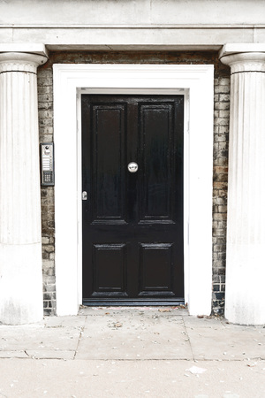 Black vintage wooden door entrance with a silver knocker and white stone columns set in brickwork