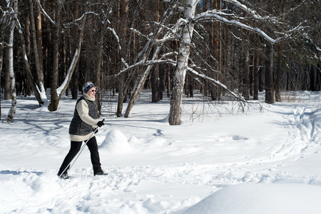 UFA, RUSSIA 29TH MARCH 2018 - Elderly woman wearing winter sports clothing cross country skiing through a forest track in snowfall using the winter sport to improve her health whilst enjoying wintry natureのeditorial素材