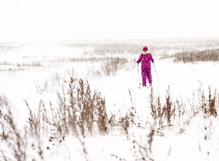 UFA, RUSSIA, 1ST APRIL 2018 - Young woman dressed in purple snow clothes and suit cross country skiing in a strong snow blizzard in a wintry snow swept scene and cold temperatures as part of her winter exercise regimeの写真素材