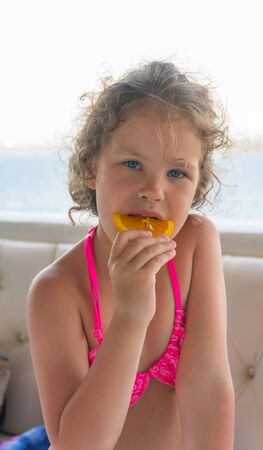 Baby with orange. Happy little girl eating orange near the sea.の写真素材