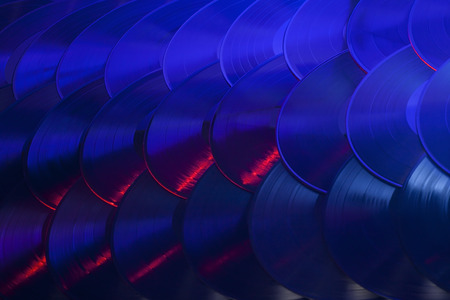 Several vinyl records overlapping in an organized array and lit with red, blue, purple and white lights の写真素材