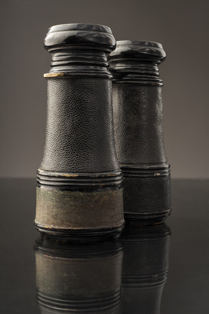 Antique binoculars sitting on its head and reflected on a dark surface.の写真素材