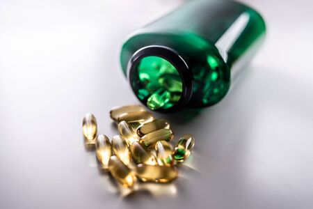 yellow pill capsules spilled out of a green plastic bottle. fish oil. vitamin E. omega-3. on white backgroundの写真素材