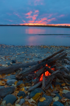 Lit campfire on the shore of Talkeetna river with red sunsetの写真素材