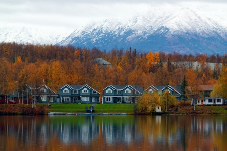Houses on shore of lake in Wasilla with orange trees and high mountain in autumnの写真素材