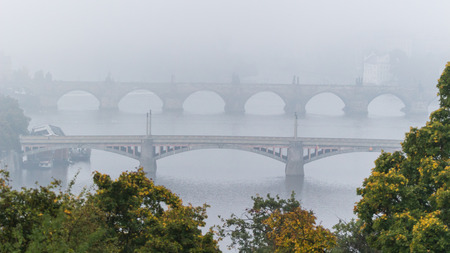 Manes and Charles bridge over Moldau (Vltava) river in morning mist with treesの写真素材