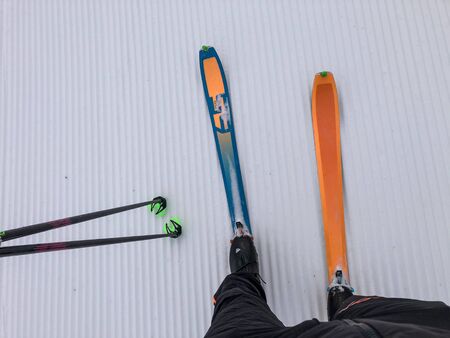 Colorful ski with legs in ski shoes and ski poles on nice ski slope. Skitouring set ready to go on nice prepared ski slope. White prepared snow ready to go down.の写真素材