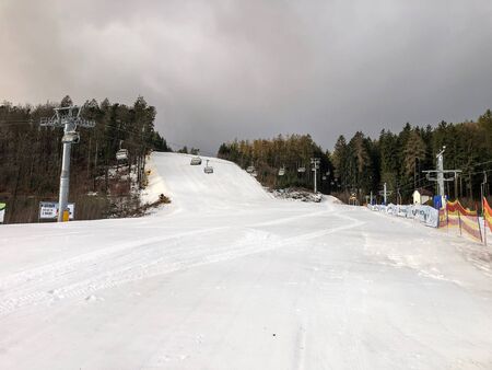Empty ski slope with snow and cableway in the Czech mountains. There is a lot of snow and nice sky with clouds and sun.の写真素材