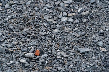 Surface full of small gray stones and a piece of orange brick. The brick is on the left lower side of the photo.の写真素材