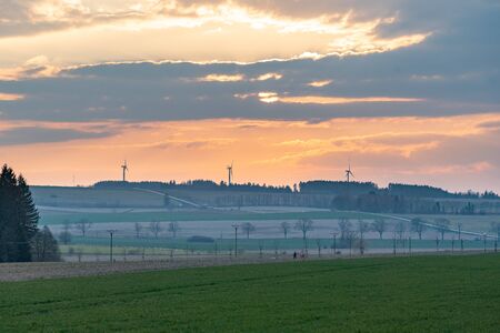 Setting sun with clouds above hills with road and wind turbinesの写真素材
