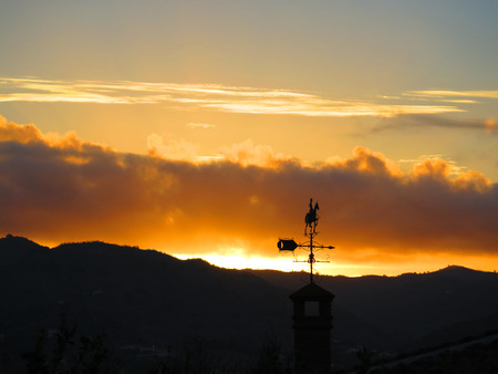 Silhouette of hills, weather wane and bright clouds at dawn near Alora Andaluciaの写真素材