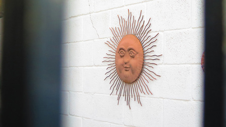 Decorative sun on white wall seen through cast iron fenceの写真素材