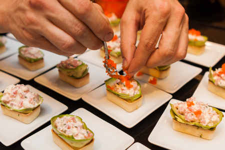 cook put red caviar on prepared delicious gourmet canapé starters on white platesの写真素材
