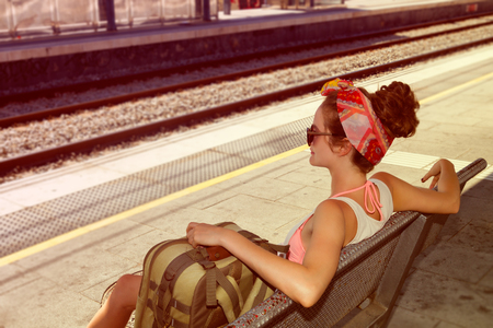 Young sexy woman backpacker sitting on bench on railway station. Travel concept.の写真素材