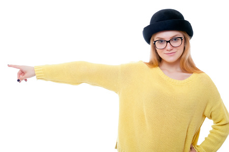 Teenage girl or young woman in yellow sweater and black hat pointing finger to the left and smilingの写真素材