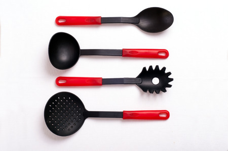 Cutlery on table. Black and red kitchenware on white tablecloth. Spoon, soup ladle, skimmer, Spoon...