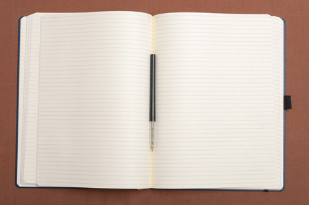 Blank notebook and black pen on brown backgroundの写真素材