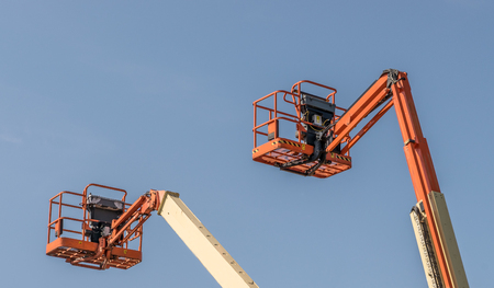 Two Cherry Picker machines against a blue skyの写真素材