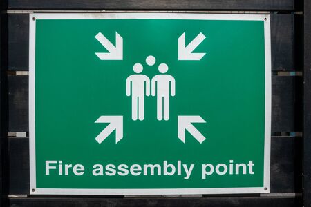 Fire Assembly Point sign attached to a black painted wooden fenceの写真素材