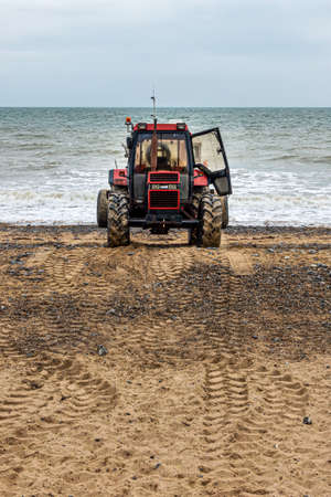 Old red tractor on a beach with the sea in the backgroundの写真素材