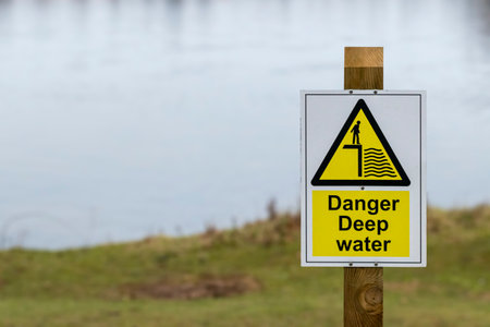 Danger Deep Water sign on a wooden post next to a lakeの写真素材