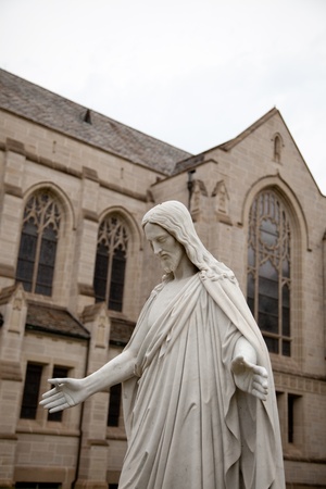 Cloase up of a marble statue of Jesus with arms outstretched and church in background の写真素材