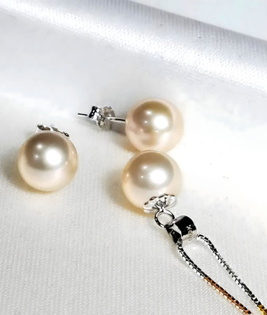 A classic and timeless jewelry set featuring a delicate pearl pendant necklace and matching earrings. The pearls are a beautiful shade of cream and are set in a simple elegant design.の写真素材