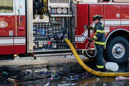 Kent, WA, USA November 14, 2016: A yellow fire hose attached to pumping station of fire engine and a fireman for Kent Fire Dept retrieving equipmentのeditorial素材