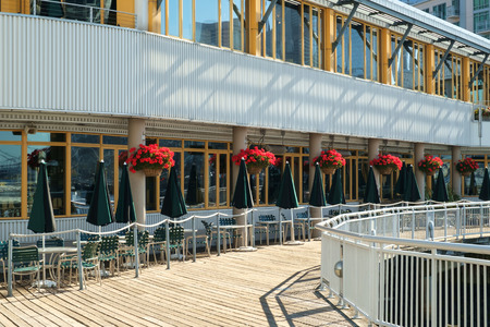 Outdoor dining area on wood deck with closed green and black umbrellas and colorful hanging flower pots.のeditorial素材