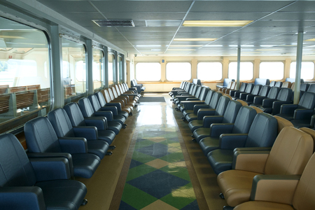 Rows of seats in passenger cabin on ferry boat with row of bright windows in backgroundのeditorial素材