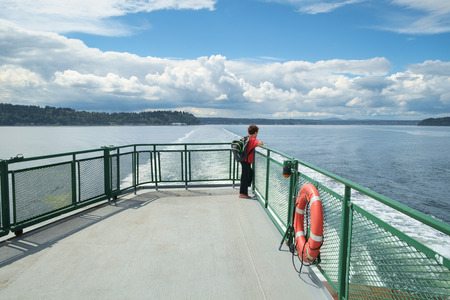 Seattle, USA August 8, 2016: Young boy wearing orange shirt and backpack looks out onto Puget Sound from deck of ferry boatのeditorial素材