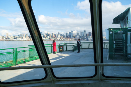 Seattle, WA, USA Feb. 11, 2017: Woman in long red coat having her picture taken on deck of ferry boat as it approaches Seattle, WAのeditorial素材