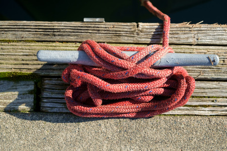 Braided red nylon boat line tied to gray cleat on dock at Des Moines, Washington marina