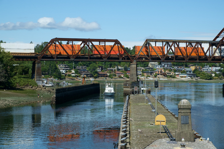 Seattle, USA July 20, 2016: Pleasure boat passes beneath Salmon Bay bridge as train crosses above with orange freight carsのeditorial素材