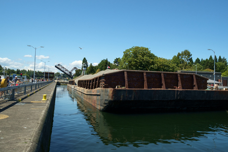 Seattle, USA July 20, 2016: Barge loaded with sand and gravel tied up in Hiram Chittenden (Ballard) Locks. Elevated wheelhouse of pusher tugboat allows clear view over bargeのeditorial素材