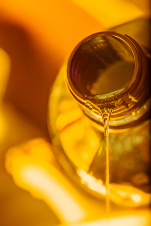 Liquid stream of motorcycle motor oil flows from the neck of the bottle close-up.