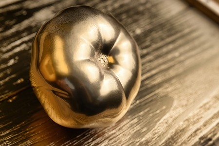 Gold painted tomato on golden and wooden backgroundの写真素材