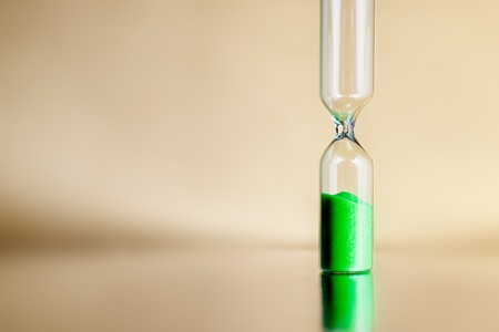 Modern beautiful green hourglass with bright background for copy space. Hourglass time passing concept for business deadline, urgency and running out of timeの写真素材