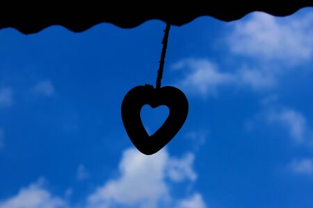 Silhouette of heart shaped wind chimes hanging from the roof of the houseの写真素材