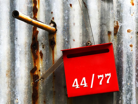 A red mailbox hangs in front of a house in a rural area of Thailandの写真素材