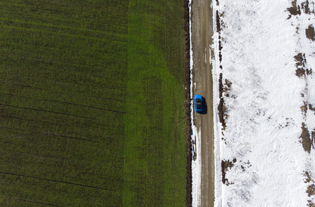aerial view of green spring field and snow from the drone. car in the road sceneの写真素材