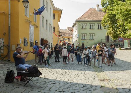 SIGHISOARA, ROMANIA - AUGUST 7 2019: Asian tourists listening to local Romanian man singing and...