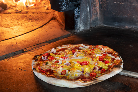 Close up pizza in firewood oven with flame behindの写真素材