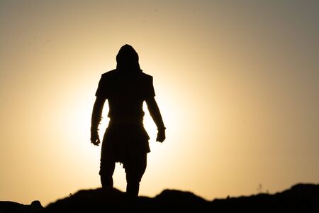 Sillhouette of a Man Standing on a Mountain Peak at the Sunsetの写真素材