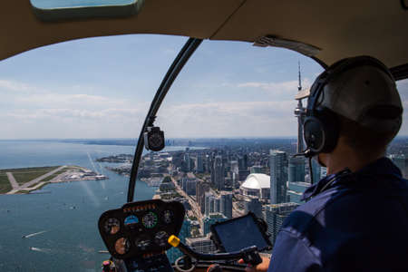 Inside view of a helicopter in flight, with man pilot. Downtown city landscape of Toronto on a sunny...