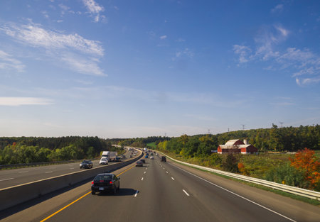 Highway through the countryside. Traffic on the road - cars and trucks. Old farm with water tower and barnのeditorial素材